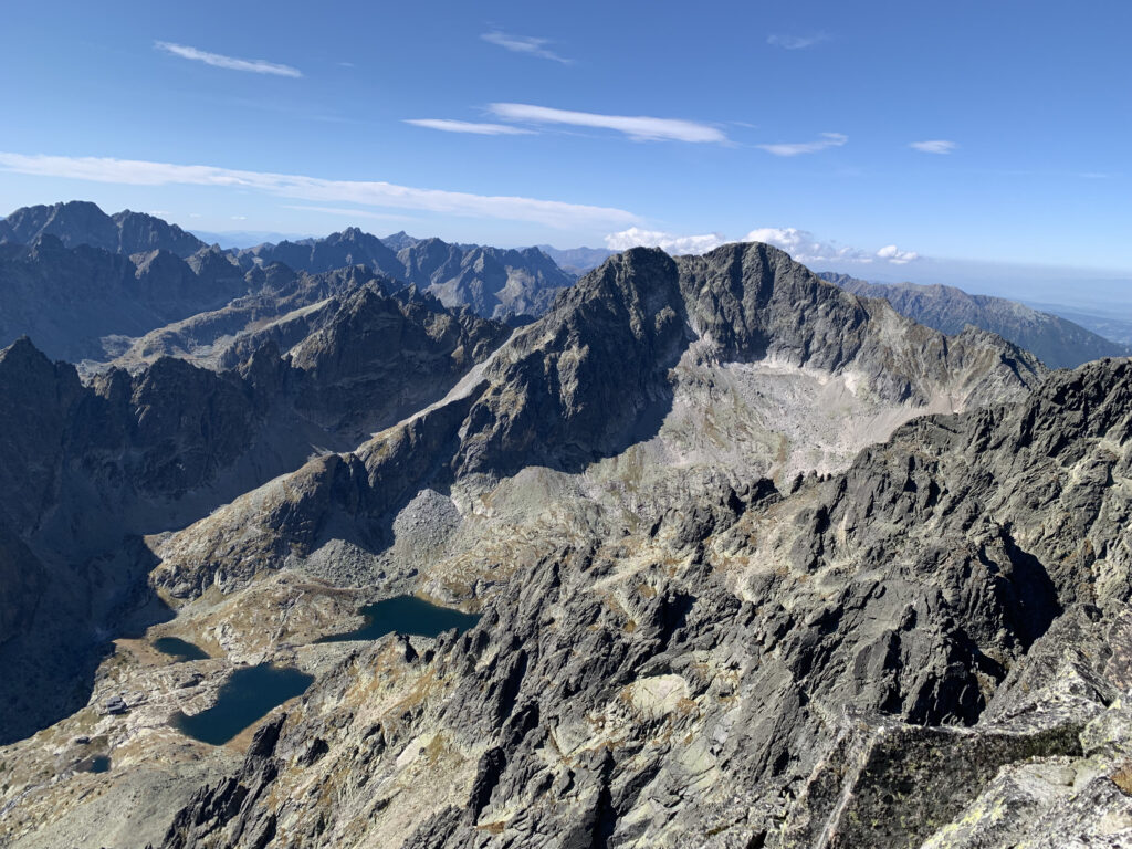 Mountain landscape with sharp rocky peaks, alpine lakes, and a large glacial cirque under a clear blue sky
