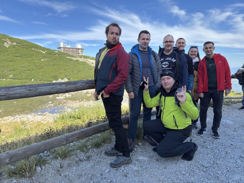 Group of colleagues posing playfully during a mountain hike with an observatory building visible in the background