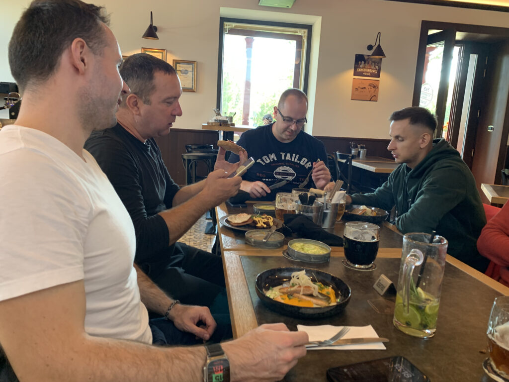 Group of colleagues sharing a meal and conversation at a restaurant table, with various drinks and dishes in front of them.