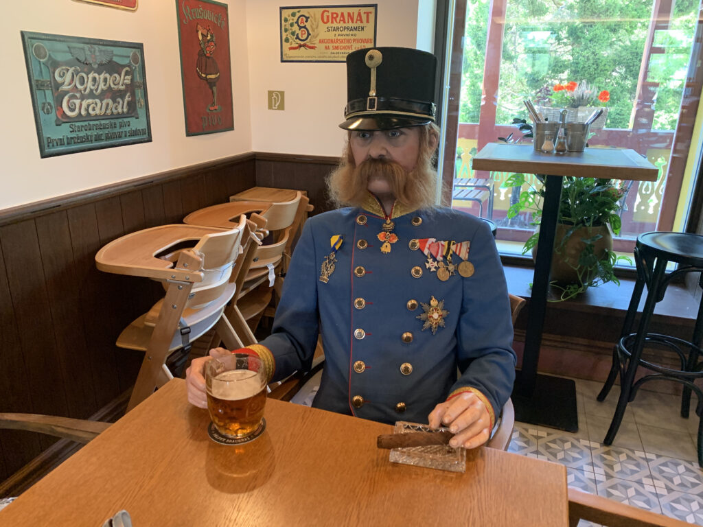 A life-sized figure of a historical soldier in full uniform with medals, sitting at a table in a vintage-style pub, holding a beer and a cigar.