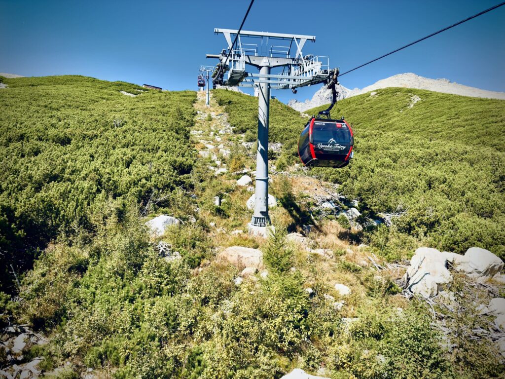 A red cable car labeled "Vysoké Tatry" ascending a green mountain slope under a clear blue sky.