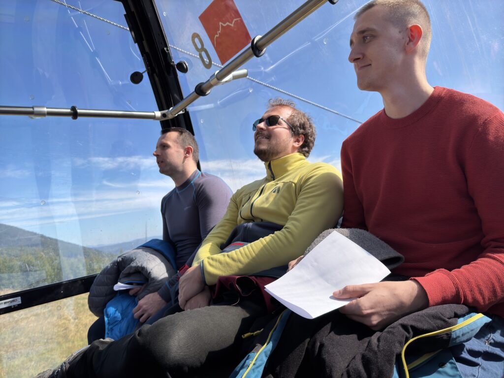 Three men sitting inside a cable car, enjoying the mountain view through large windows on a sunny day