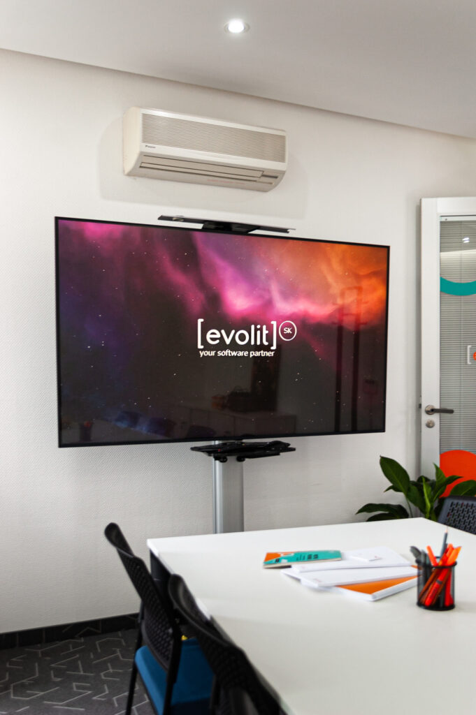 Modern conference room at Evolit with a large screen displaying the company logo, a white meeting table with notebooks and pens, and a plant in the corner.